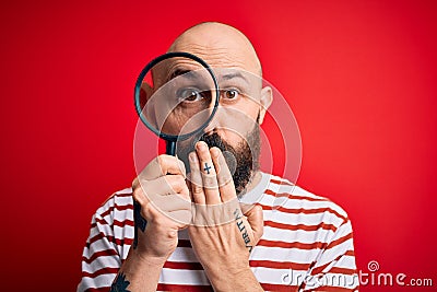 Handsome detective bald man with beard using magnifying glass over red background cover mouth with hand shocked with shame for Stock Photo