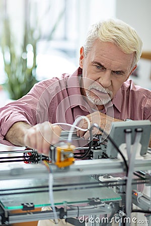 Handsome elderly man adjusting extruder of 3D printer Stock Photo