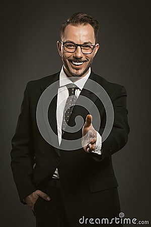 Handsome entrepreneur giving hand to handshake. Friendly businessman smiles holding his hand forward expresses a Stock Photo