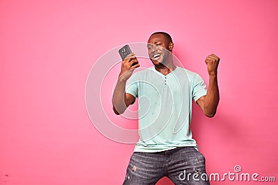 handsome excited young black man feeling excited while viewing content on his smartphone, celebrating winning Stock Photo