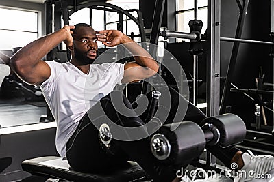 Handsome fit african man in sportwear doing crunches using a bench at gym. Stock Photo