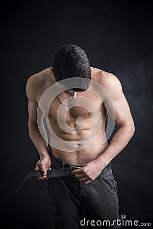 Handsome, fit shirtless young man undoing pants' belt Stock Photo