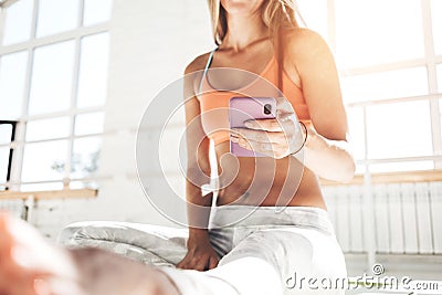 Handsome fit woman sitting on yoga mat and hold smartphone in hand counts calories in fitness application after training Stock Photo