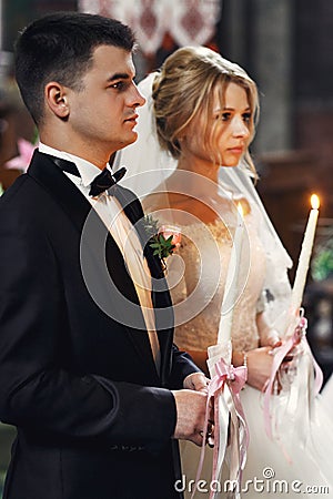Handsome groom in suit and a beautiful blonde bride holding candles in church close-up Stock Photo