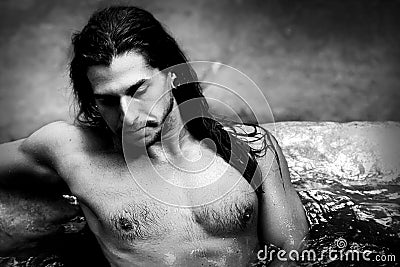 A handsome guy with long hair and piercings on waterfalls in a rain forest. Tarzan concept. Black and white photo. Stock Photo