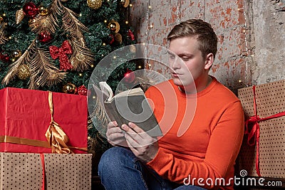 Handsome guy is reading a book sitting under the tree surrounded by boxes of gifts. Christmas and gifts Stock Photo