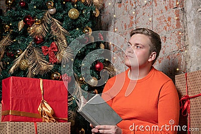 Handsome guy is reading a book sitting under the tree surrounded by boxes of gifts. Christmas and gifts Stock Photo