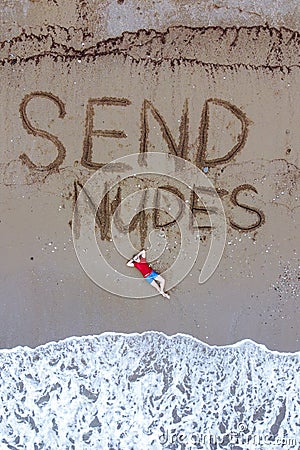 Handsome guy in red t-shirt and blue male boxers is lying on beach washed by foaming sea waves. send nudes inscription on wet sand Stock Photo