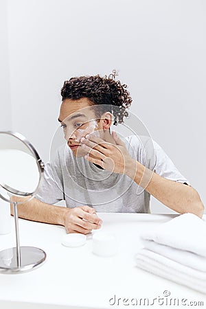 handsome guy sit in front of the mirror, facial skin care light background Stock Photo