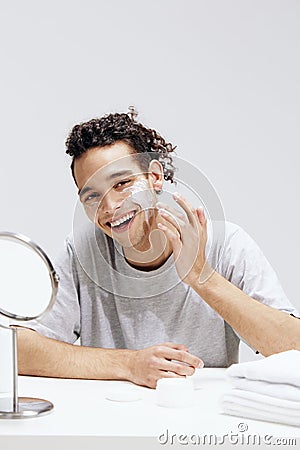 handsome guy sit in front of the mirror, facial skin care light background Stock Photo