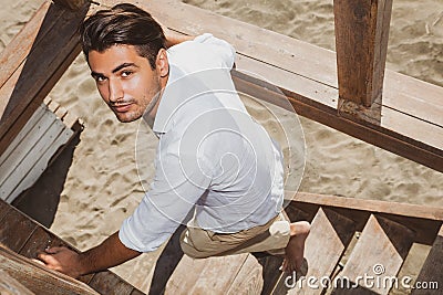 Handsome guy with trendy hairstyle going down wooden stairs while looking. Stock Photo