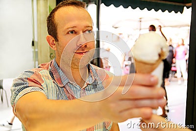 Handsome happy man sells ice cream in shop. Kind female seller in candy store gives ice cream to boy. Stock Photo