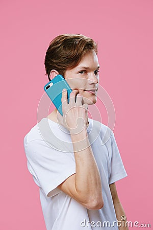 handsome happy young man teenager in white t-shirt stands talking on the phone in blue case looking at camera on pink Stock Photo