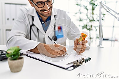 Handsome hispanic man working as doctor writing pills presciption at hospital clinic Stock Photo