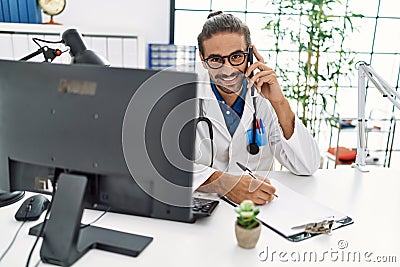 Handsome hispanic man writing presciption on the phone at hospital clinic Stock Photo