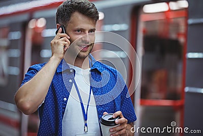 Handsome holding disposable cup while talking on mobile phone Stock Photo