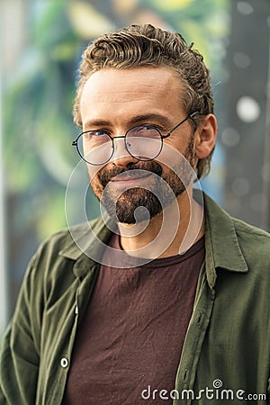 Handsome individual wearing glasses, situated outdoors against a graffiti-covered background. With a stylish and Stock Photo