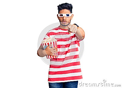 Handsome latin american young man wearing 3d glasses and eating popcorn at the movies pointing with finger to the camera and to Stock Photo