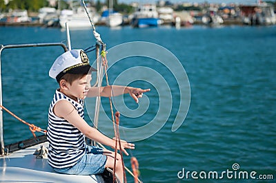 Handsome little captain boy pointing with his finger to the distance sitting on luxury yacht in summer tour Stock Photo