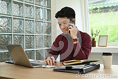 Handsome male investment advisor using laptop and talking on mobile phone with client Stock Photo