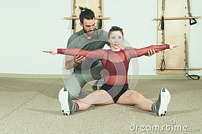 Handsome male personal trainer with a beard helping young fitness girl to stretch her muscles after hard training workout, selecti Stock Photo