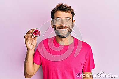 Handsome man with beard holding pink geode precious gemstone looking positive and happy standing and smiling with a confident Stock Photo