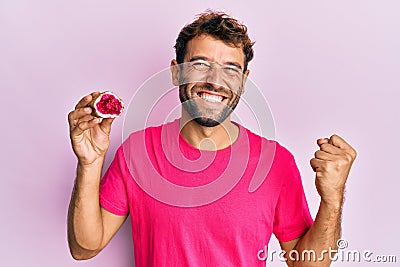 Handsome man with beard holding pink geode precious gemstone screaming proud, celebrating victory and success very excited with Stock Photo