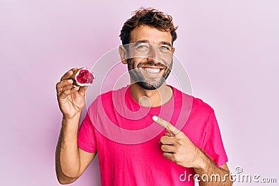 Handsome man with beard holding pink geode precious gemstone smiling happy pointing with hand and finger Stock Photo