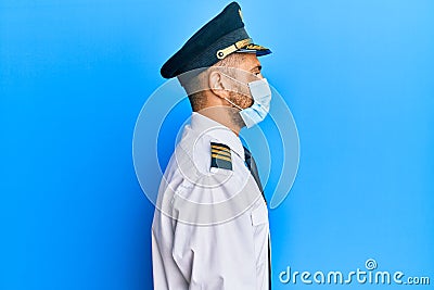 Handsome man with beard wearing airplane pilot uniform wearing safety mask looking to side, relax profile pose with natural face Stock Photo