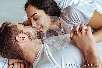 Handsome man and beautiful woman lying in bed and kissing in bedroom. Stock Photo
