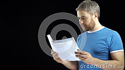 Handsome man in blue tshirt looking through papers. Cotract, bills, letter concepts. Black background Stock Photo