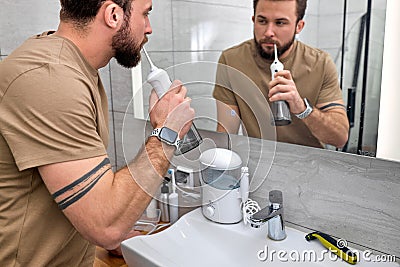 Handsome man cleans teeth using electric oral irrigator with jet of water, near mirror Stock Photo