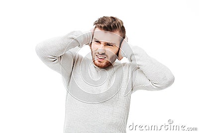 Handsome man covering ears because of loud noise over white background. Guy can`t stand the sound isolated Stock Photo