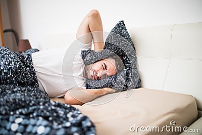 Handsome man covering his head and ears blocking out the sound with a pillow, suffering from loud alarm wake-up signal, young guy Stock Photo