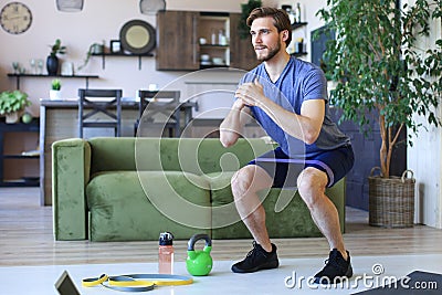 Handsome man doing squats exercise at home during quarantine. Concept of healthy life Stock Photo