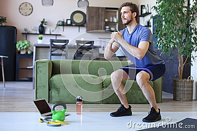Handsome man doing squats exercise at home during quarantine. Concept of healthy life Stock Photo