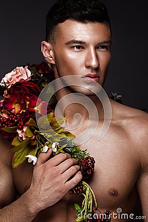 A handsome man with a naked torso, bronze tan and flowers on his body. Stock Photo