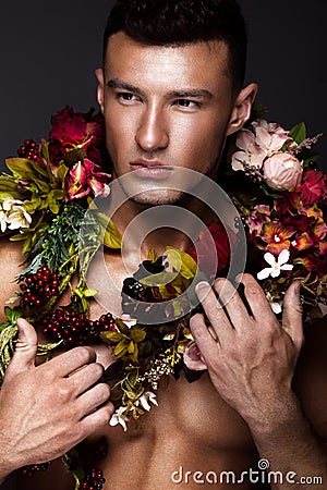 A handsome man with a naked torso, bronze tan and flowers on his body. Stock Photo