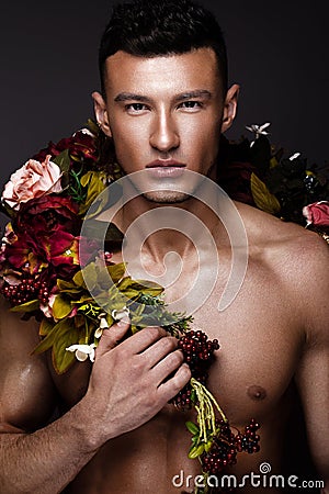 A handsome man with a naked torso, bronze tan and flowers on his body. Stock Photo