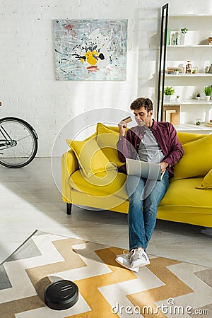 Man online shopping while robotic vacuum Stock Photo