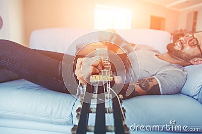 Man playing acoustic guitar lying on sofa Stock Photo