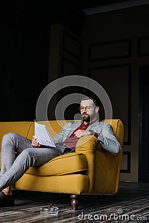 handsome man reading newspaper and sitting on couch ashtray with cigar Stock Photo