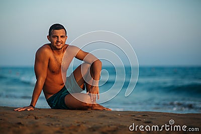 Handsome man on a sandy beach sits on the seashore. Young man on the coast Stock Photo