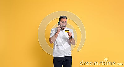 Handsome man screaming ecstatically for receiving reward while talking over smart phone and looking at credit card on yellow Stock Photo