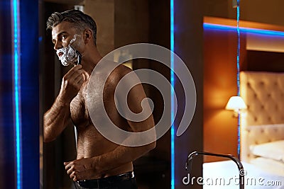 Handsome Man Shaving Face In Bathroom. Facial Hair Grooming Stock Photo