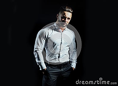 Handsome man standing with arms in pockets isolated on a black background. A handsome confident young man standing and Stock Photo