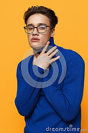 a handsome man stands in black glasses for vision in a blue zip-up jacket, posing on an orange background with his hand Stock Photo