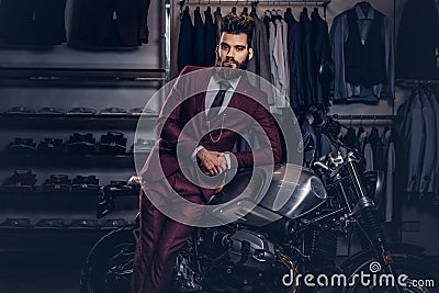 Handsome man with a stylish beard and hair dressed in vintage red suit posing near retro sports motorbike at men`s Stock Photo