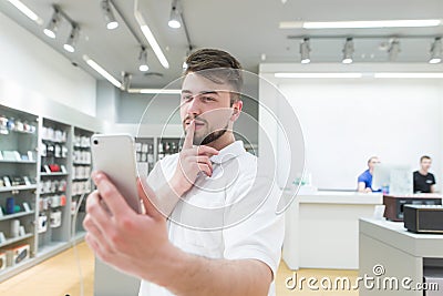 Handsome man takes a selfie on a smartphone in a tech store Stock Photo