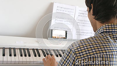 Handsome man tries to play the piano. Young man learns to play the piano with lessons on mobile phone Stock Photo